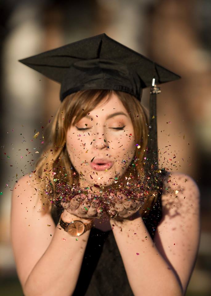 A student wearing a graduation cap blowing glitter from her hands